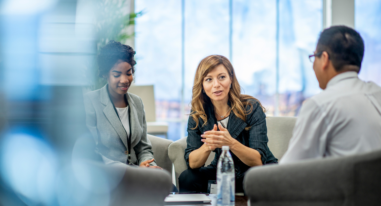 two women and one man sitting in a lobby talking dressed in casual business attire