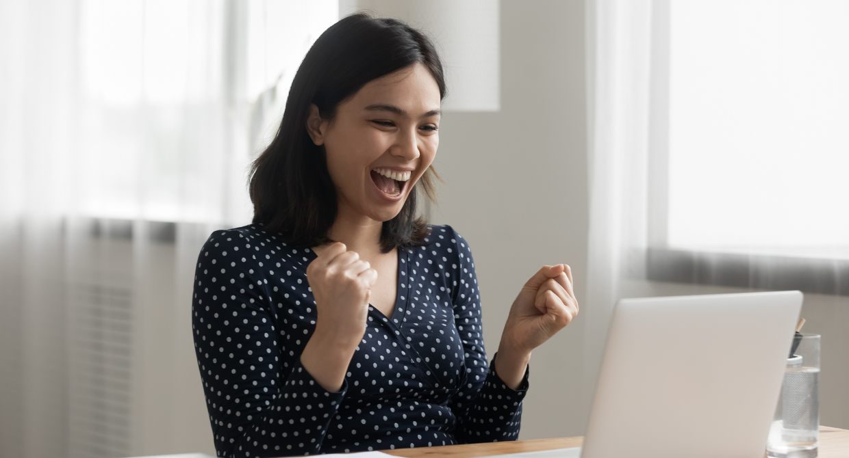 Woman celebrating with smile on her face while working with laptop in front of her in a bright and bright and airy room